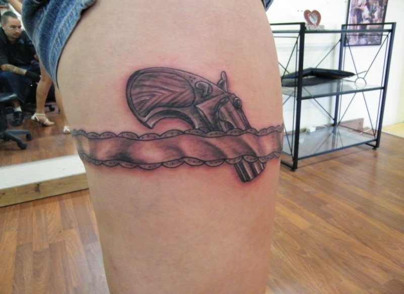 女孩大腿上的环形初边和手枪纹身图案